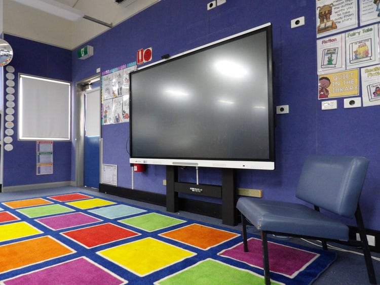An interactive whiteboard in front of a colourful mat for students to sit and learn in front of.